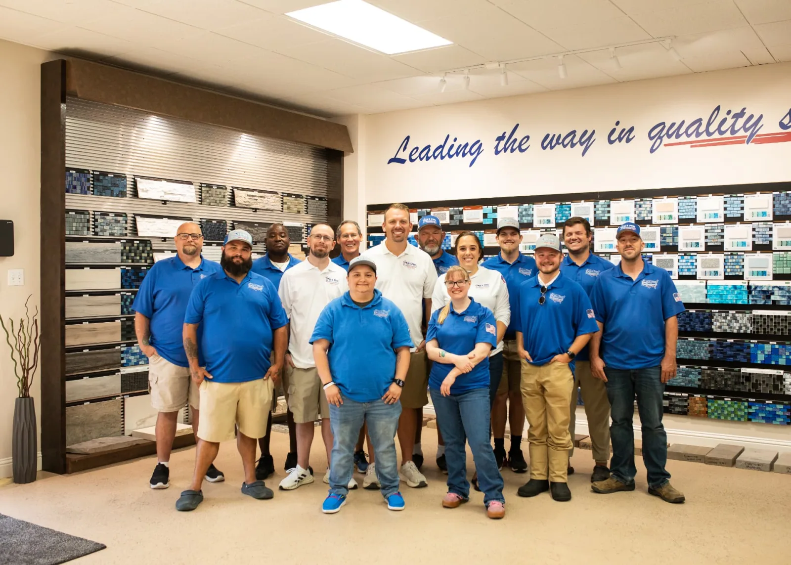 The U.S. Pool Professionals team together in the Rockwall showroom in front of the tile display wall